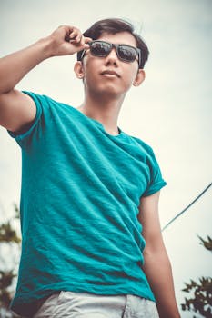 A fashionable young man wearing sunglasses poses confidently outdoors, showcasing summer style.