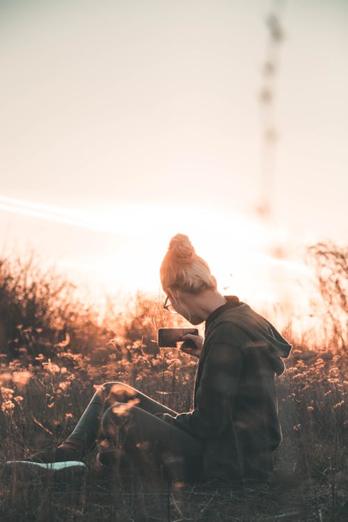 Selective Focus Photography of Woman Sitting on Ground While Holding Smartphone