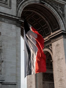 Low angle flag of France waving under Arc de Triomphe in Paris on sunny day