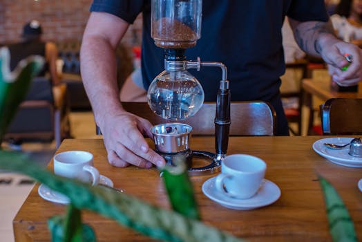 Hands engaged in brewing coffee with a siphon at a cozy café setting.