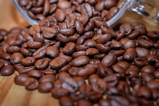 High-quality close-up image of roasted coffee beans spilling from a jar on a wooden surface.