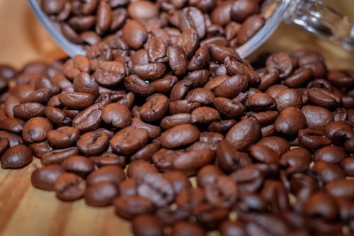 Free High-quality close-up image of roasted coffee beans spilling from a jar on a wooden surface. Stock Photo