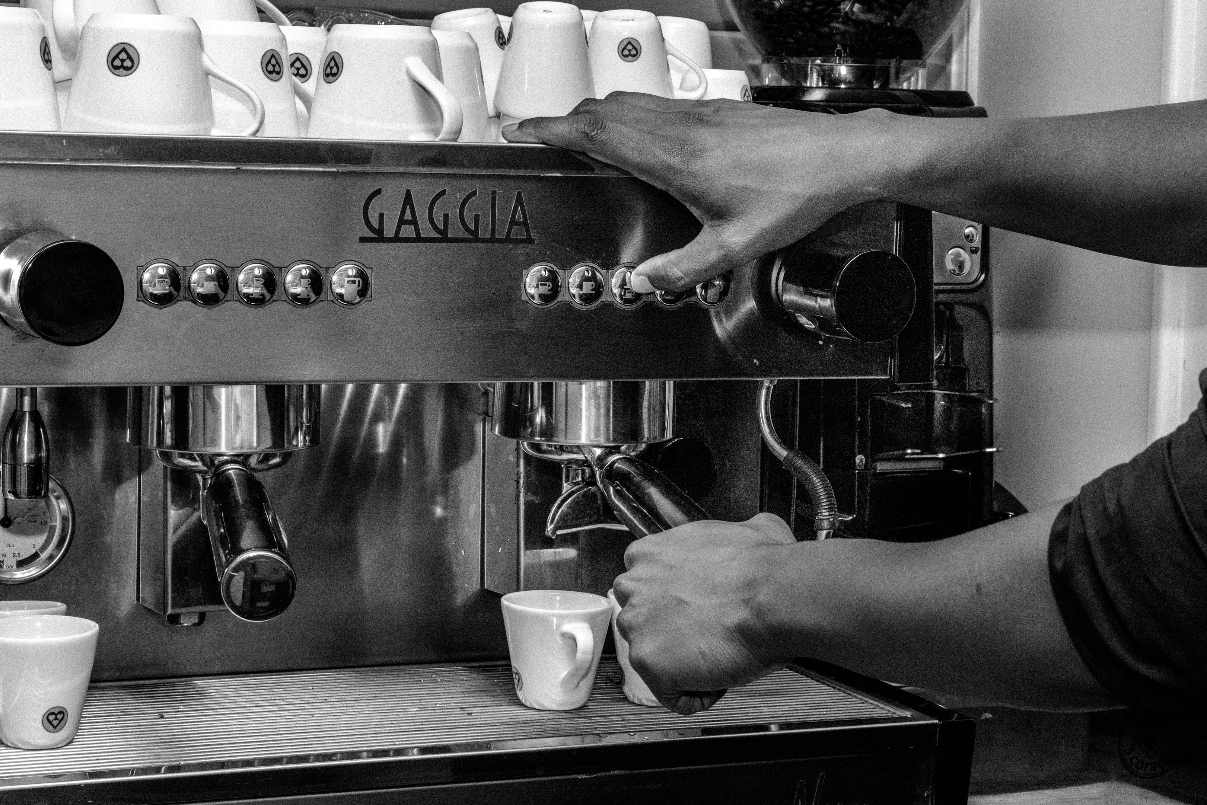 Black and white photo of a barista operating a Gaggia espresso machine in a café.