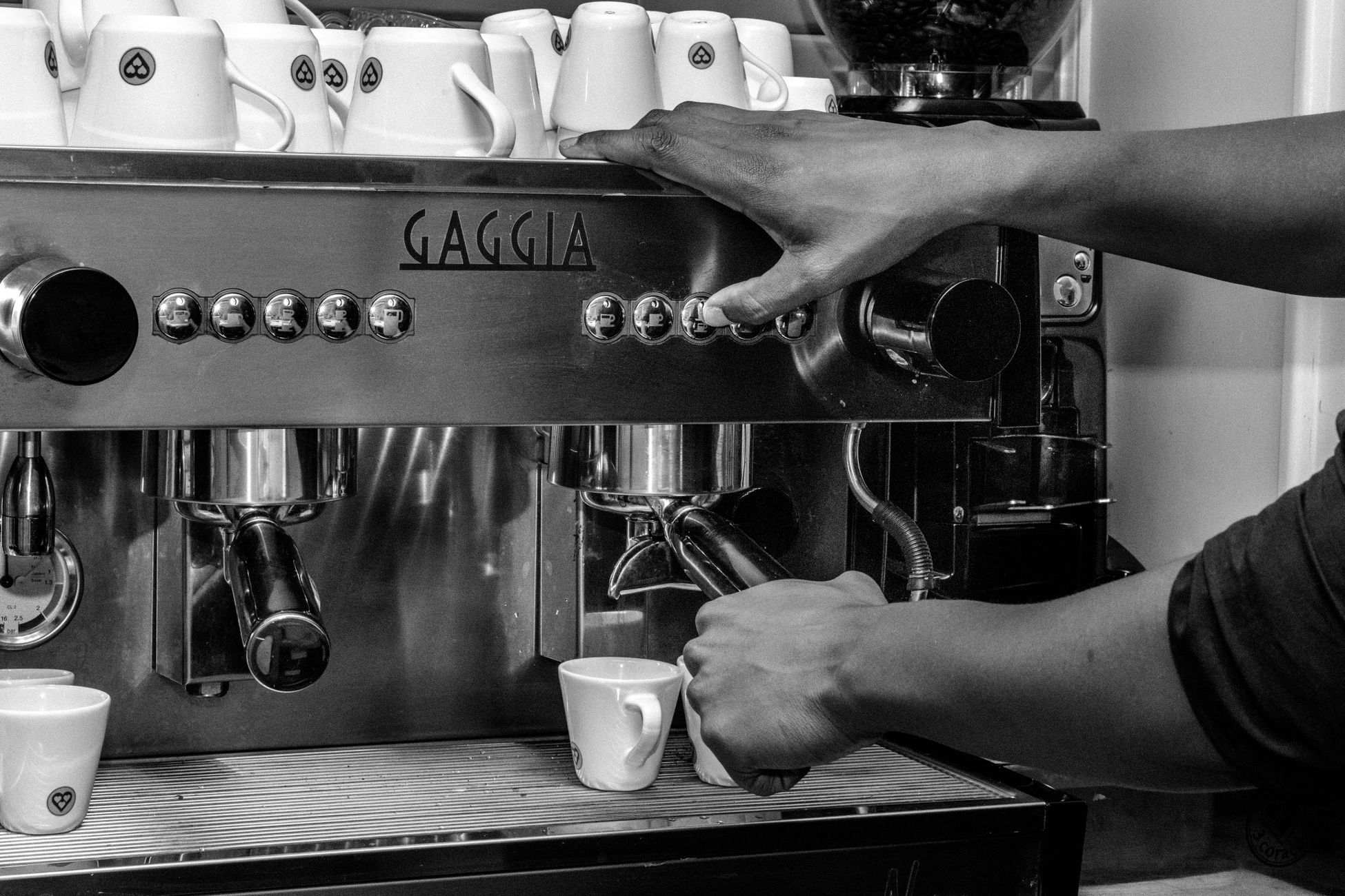 Black and white photo of a barista operating a Gaggia espresso machine in a café.