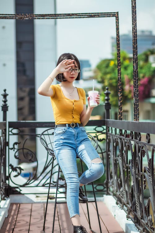 Shallow Focus Photo of Woman in Yellow T-shirt Holding Plastic Cup Sitting on Bar Chair