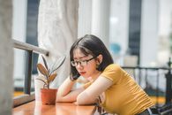一位戴着眼镜的年轻女子在室内以轻松的姿势坐在盆栽植物旁