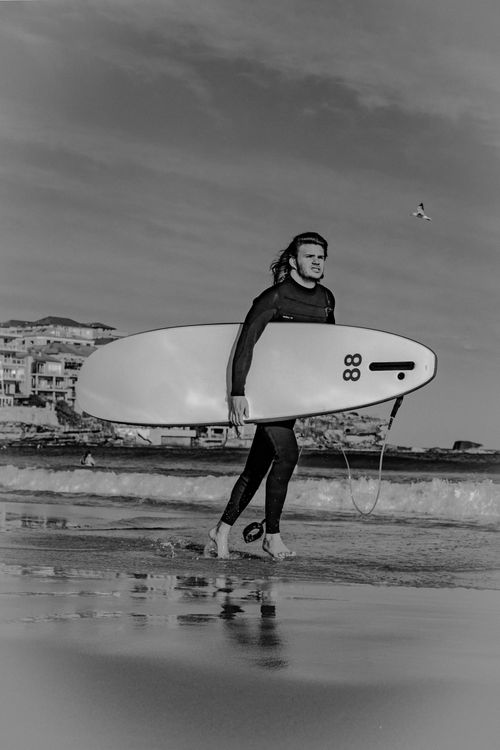 Free Black and white photo of a surfer carrying a surfboard at Bondi Beach, Australia. Stock Photo