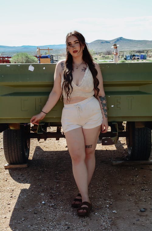 A woman in white shorts and a tank top standing next to a truck