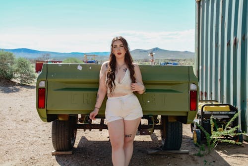 A woman in shorts and a white top stands next to a truck