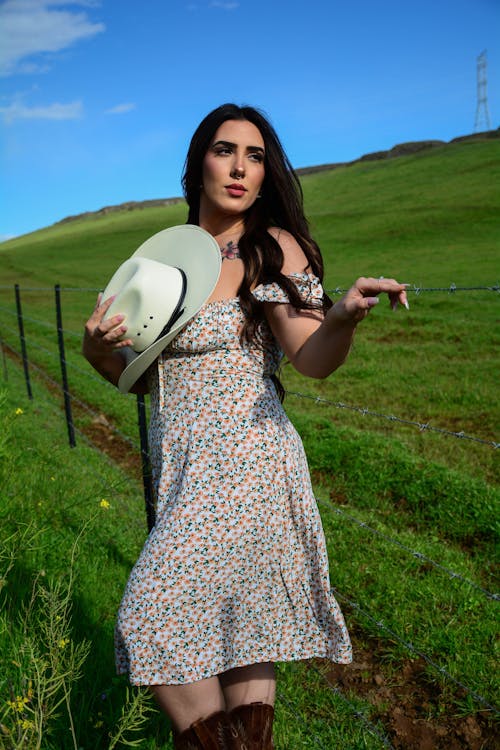A woman in a dress and cowboy hat is standing in a field