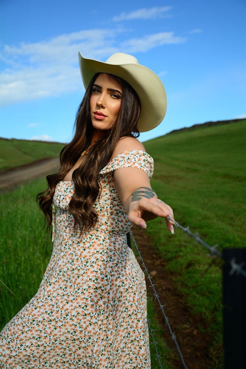 A woman in a dress and cowboy hat standing on a fence