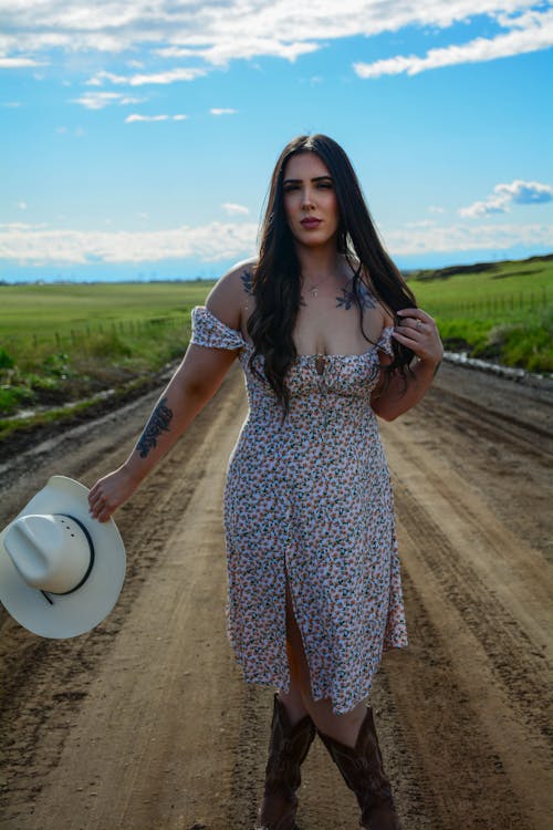 A woman in a dress and cowboy hat standing on a dirt road