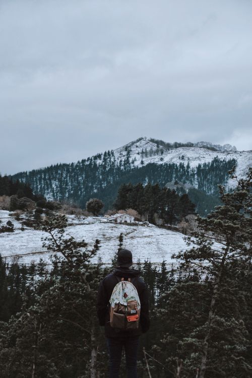 Free A lone hiker stands with a backpack, overlooking a snowy mountain landscape during a winter day. Stock Photo