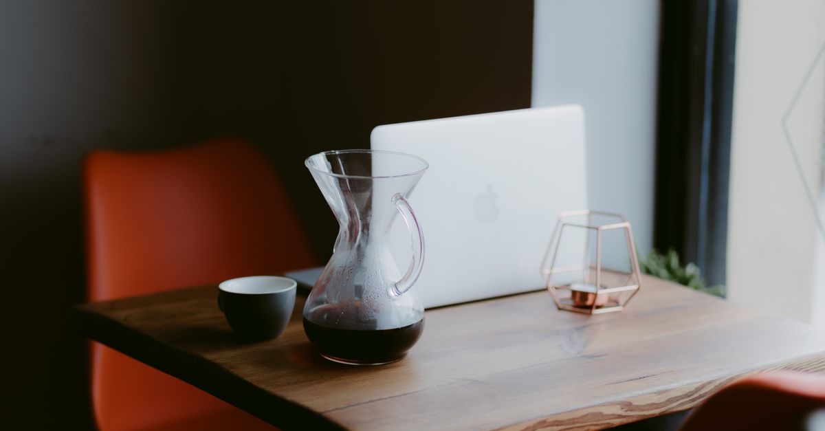 a glass of water and a cup of Ghanaian coffee on a wooden desk with a laptop