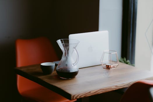 A stylish coffee shop table setup with a Chemex and laptop, ideal for relaxing or working.