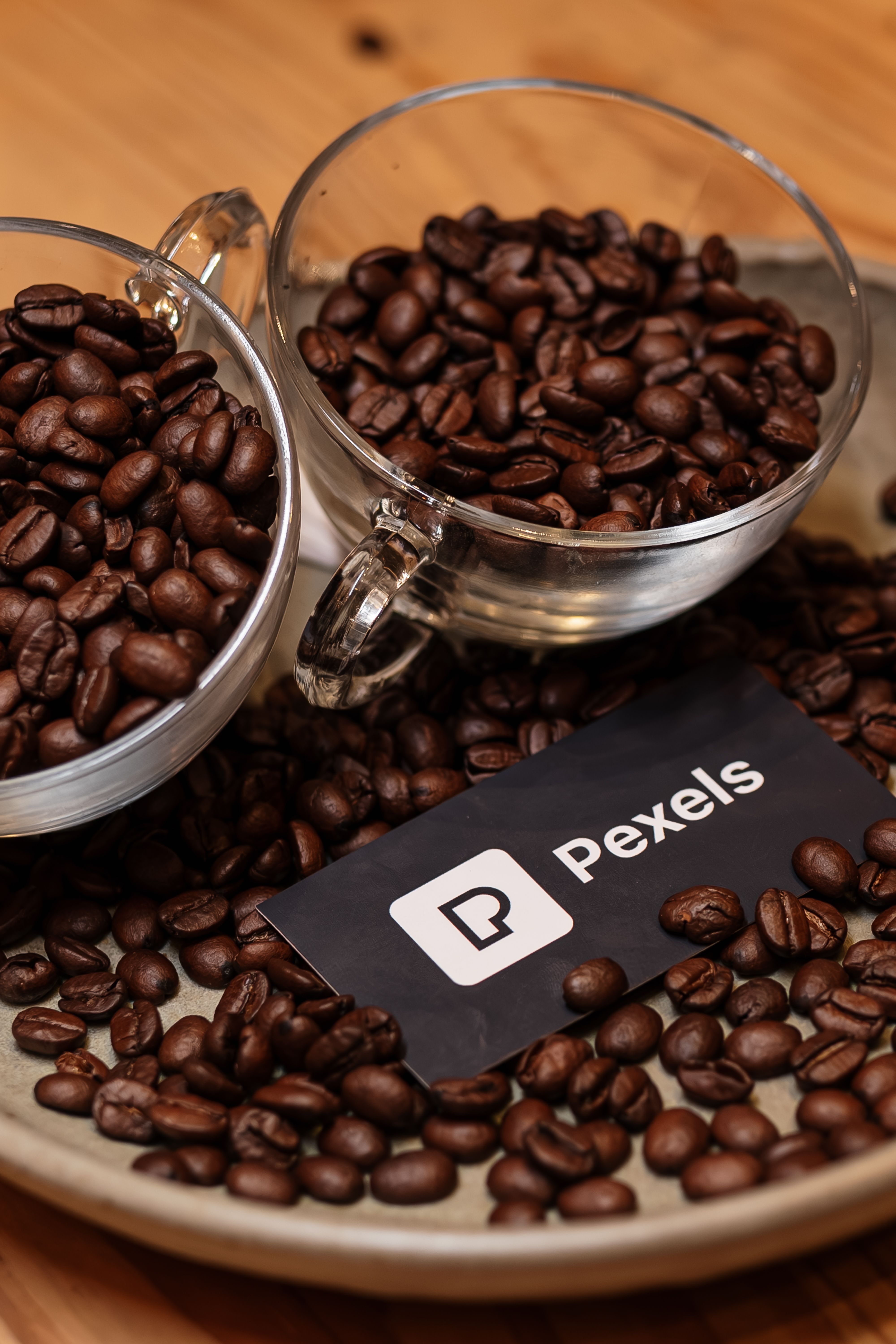 Two glass cups filled with coffee beans on a tray, featuring a Pexels card.