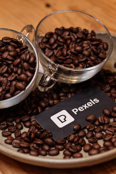 Two glass cups filled with coffee beans on a tray, featuring a Pexels card.
