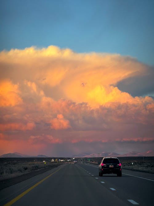 A car driving down a highway with a cloud in the sky