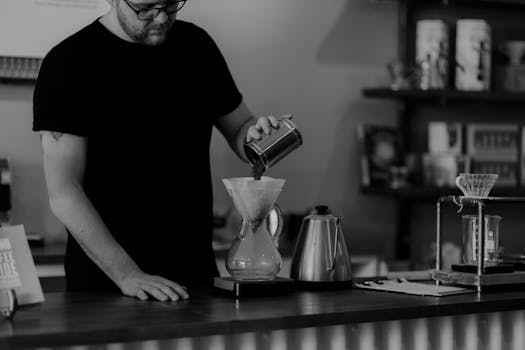 A barista prepares coffee using a Chemex in a stylish UK café, creating a perfect brew.