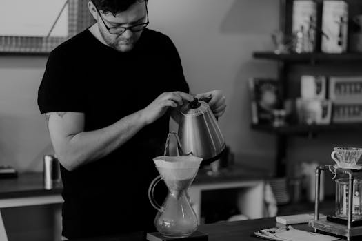 A barista skillfully prepares pour-over coffee in a modern café setting. Black and white.