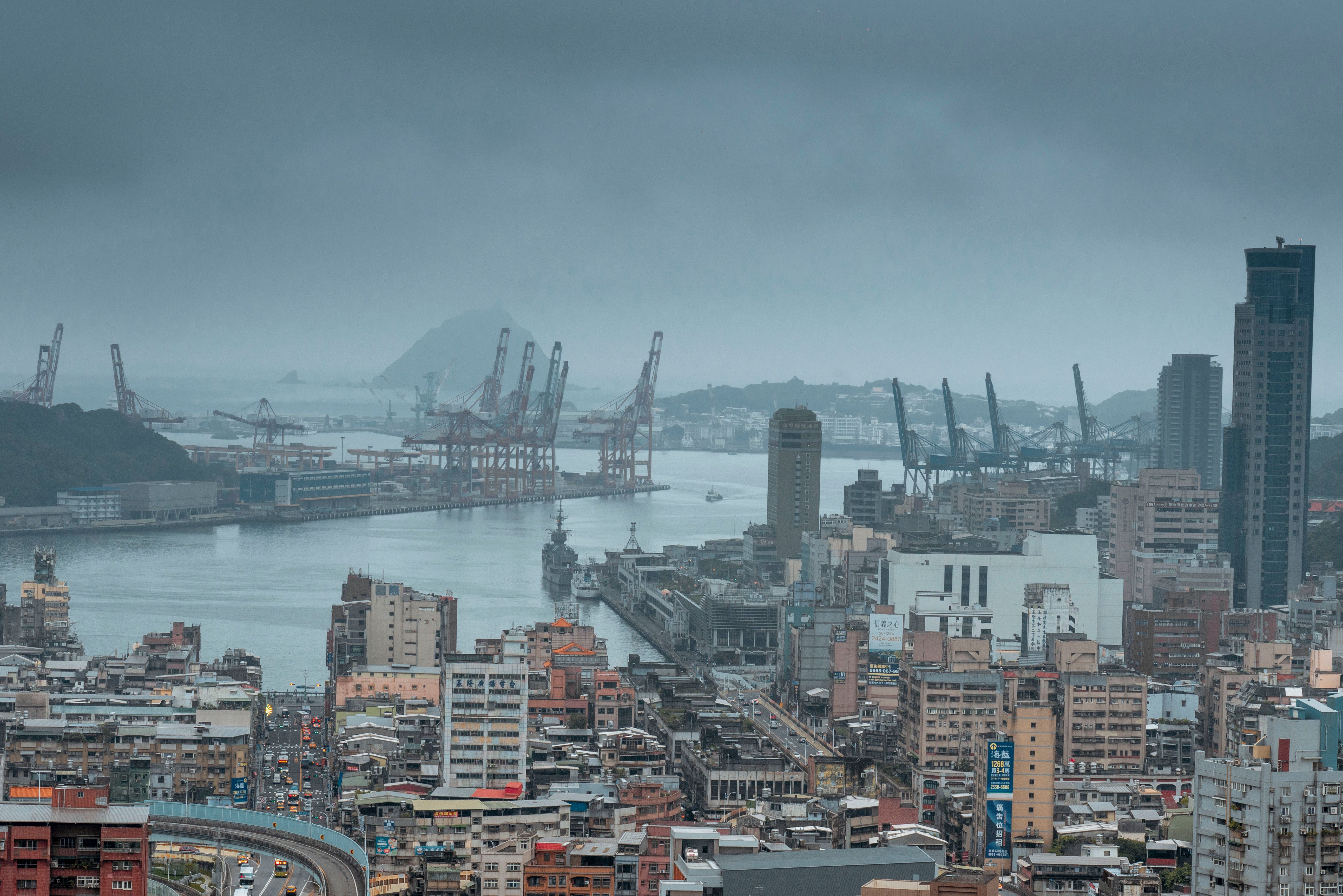 Aerial view of Keelung Harbor showcasing urban sprawl and cranes under cloudy skies.