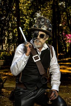 A stylish man in a steampunk outfit, holding a goblet and pistol, outdoors in a park.