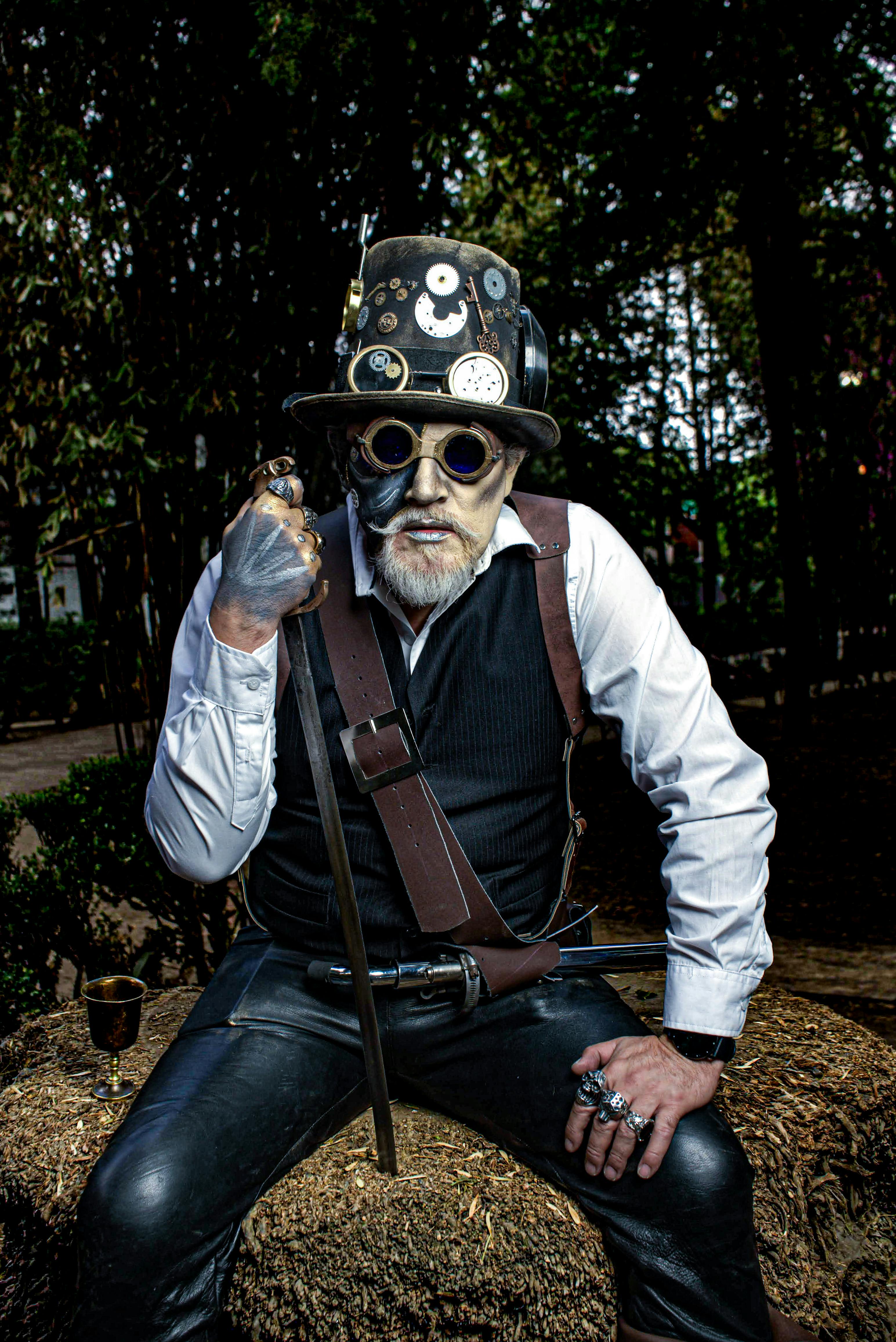 Steampunk styled man in a forest setting with top hat and goggles, holding a cane.