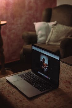 A laptop displaying a photo is set on a table in a dimly lit cozy living room.