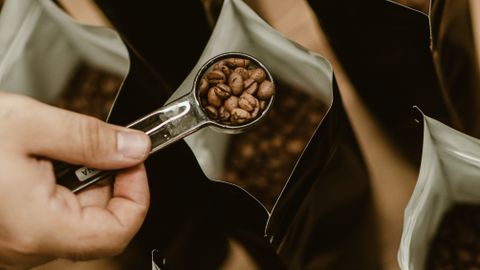 A person scooping coffee beans into bags, emphasizing fresh roasting and packaging.