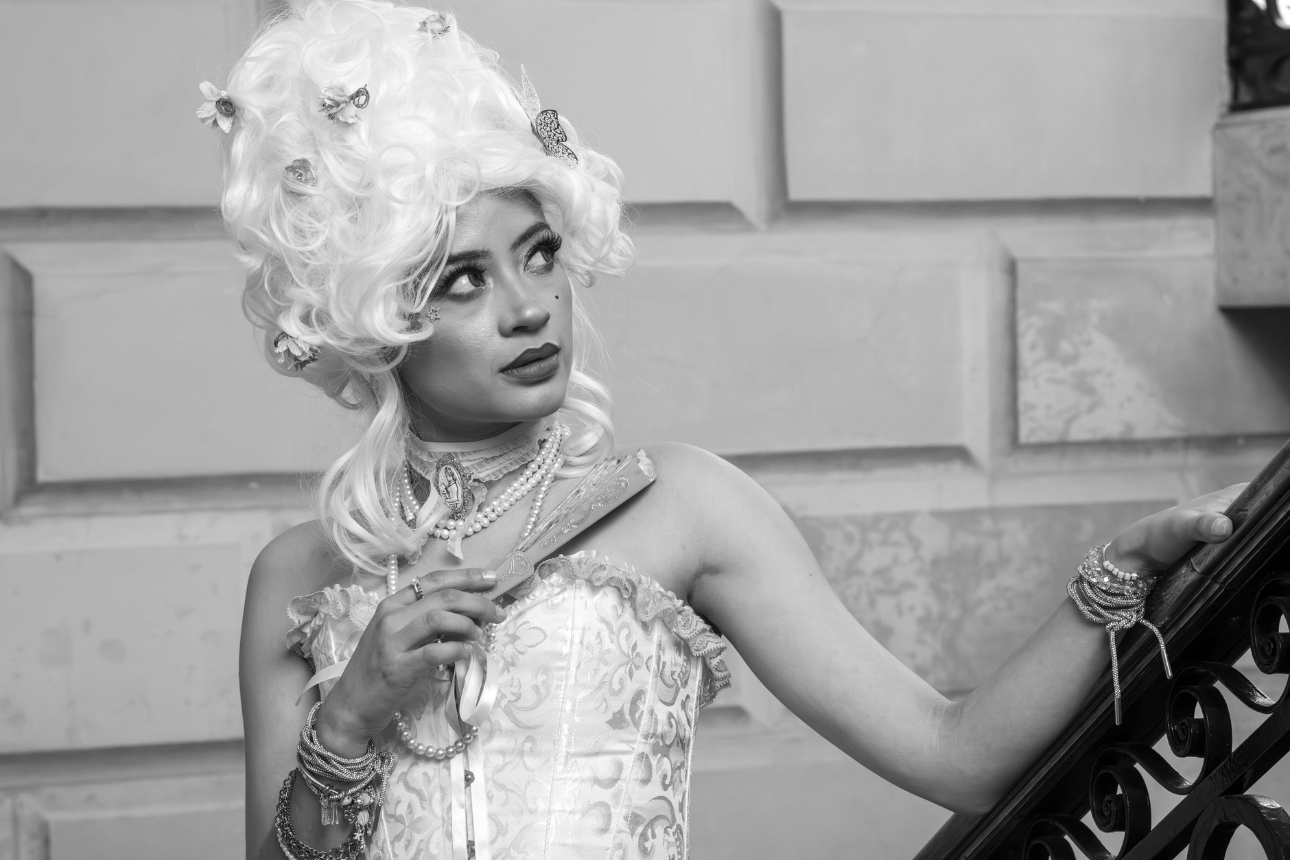 Black and white portrait of a woman in rococo fashion holding a closed fan.
