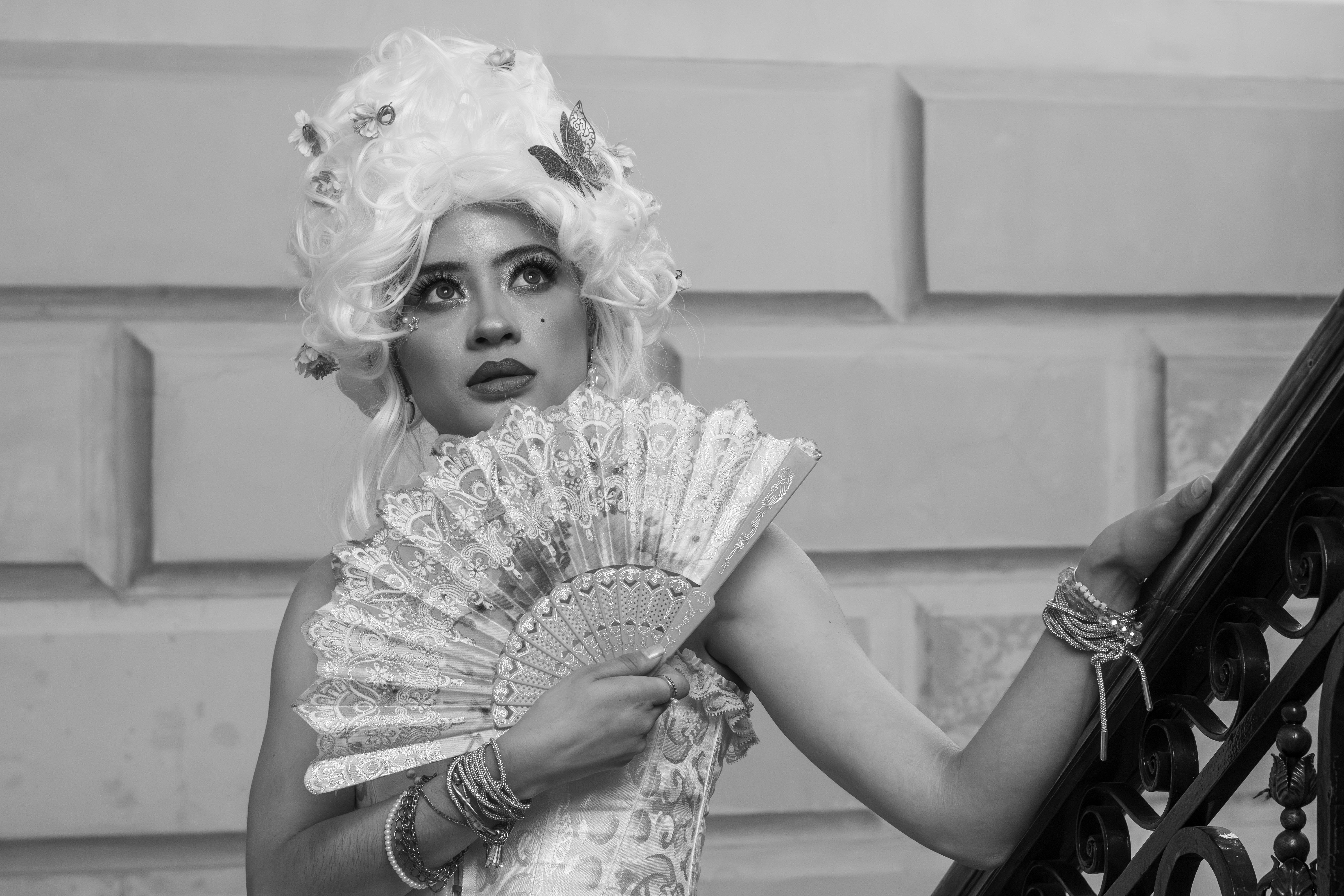 Elegant woman in rococo-inspired fashion holding a fan, black and white photography.