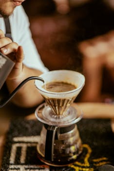Person pouring hot water through a dripper for manual coffee brewing.