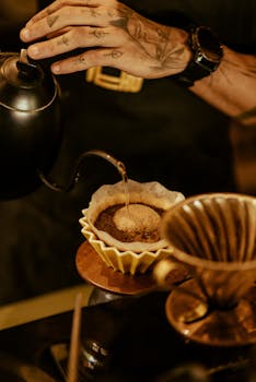 Hand pouring over coffee in filter with kettle, showcasing artisanal brewing method.