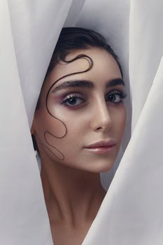 Close-up portrait of a woman with artistic hair styling, soft makeup, framed by flowing fabric.