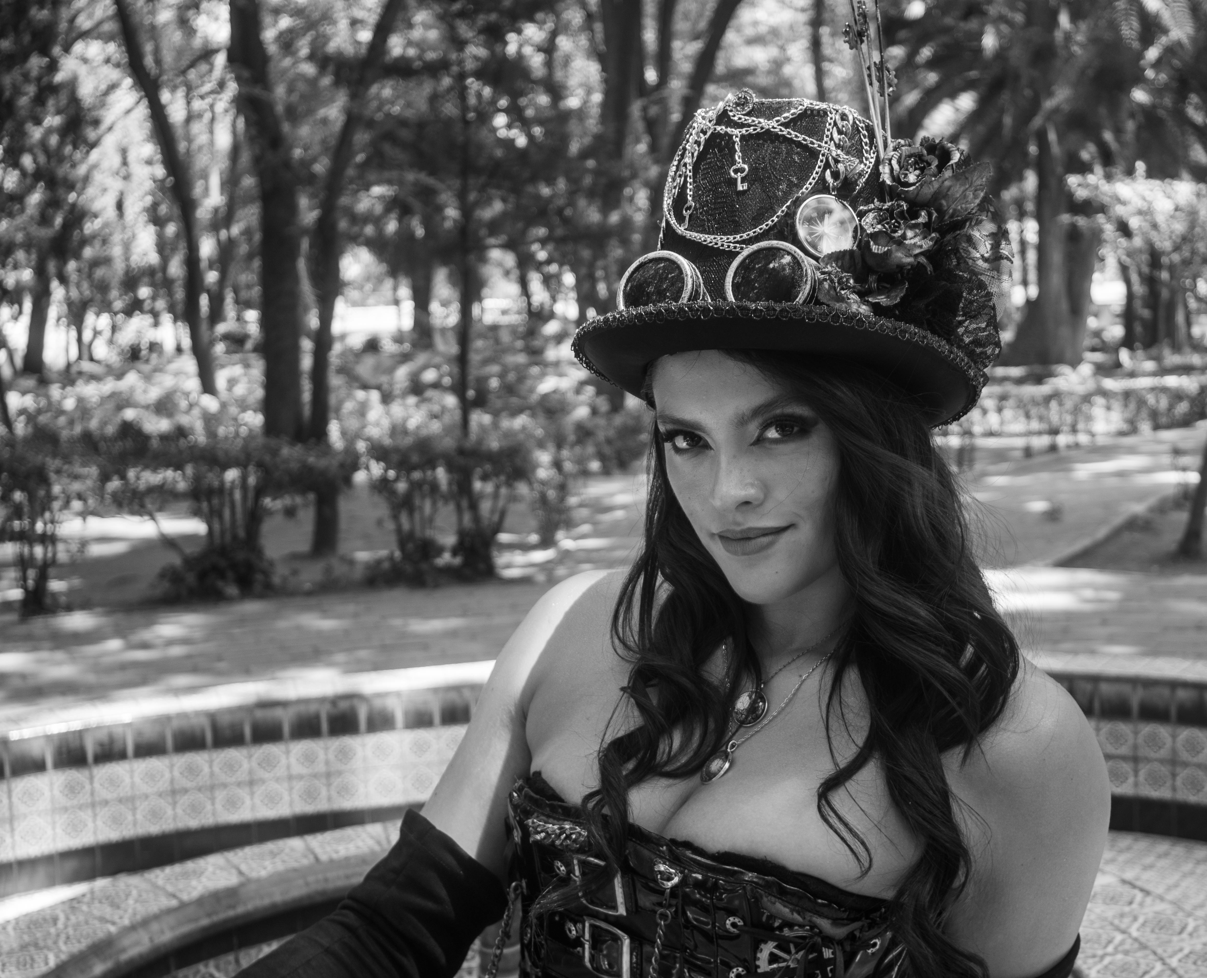 Black and white photo of a young woman in a steampunk costume posing outdoors in a park.
