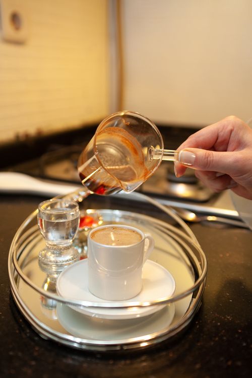 Free A hand pours coffee into a cup on a silver tray, creating a cozy coffee moment. Stock Photo