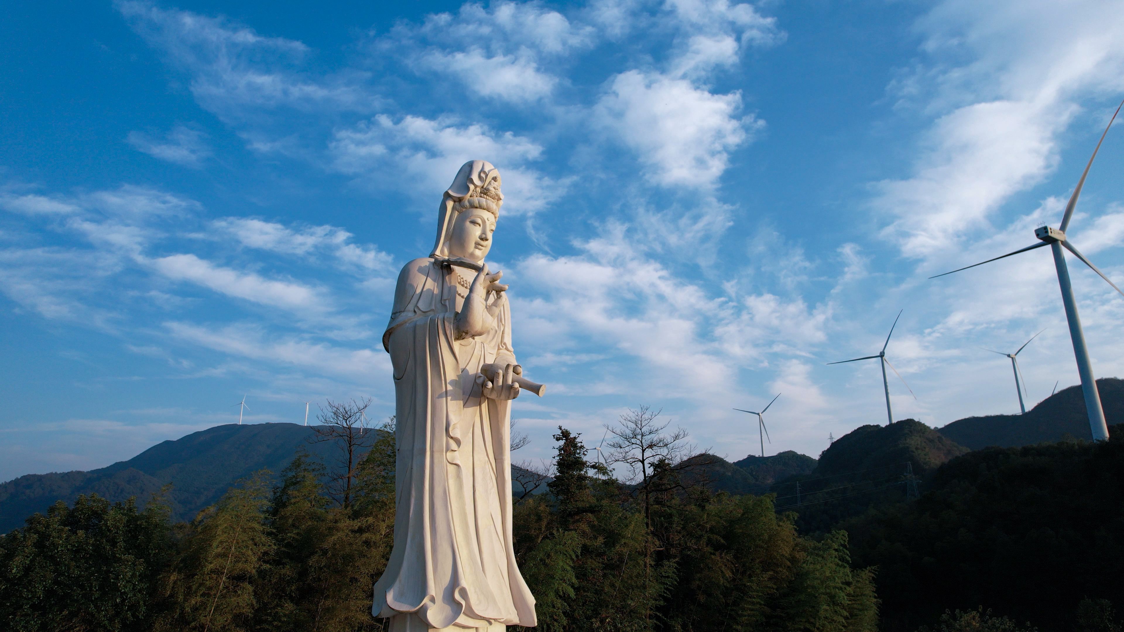 Peaceful statue with wind turbines in scenic outdoor landscape under a blue sky.