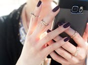 特写镜头中，一位女士指甲修剪整齐，手持智能手机，戒指点缀，尽显时尚优雅