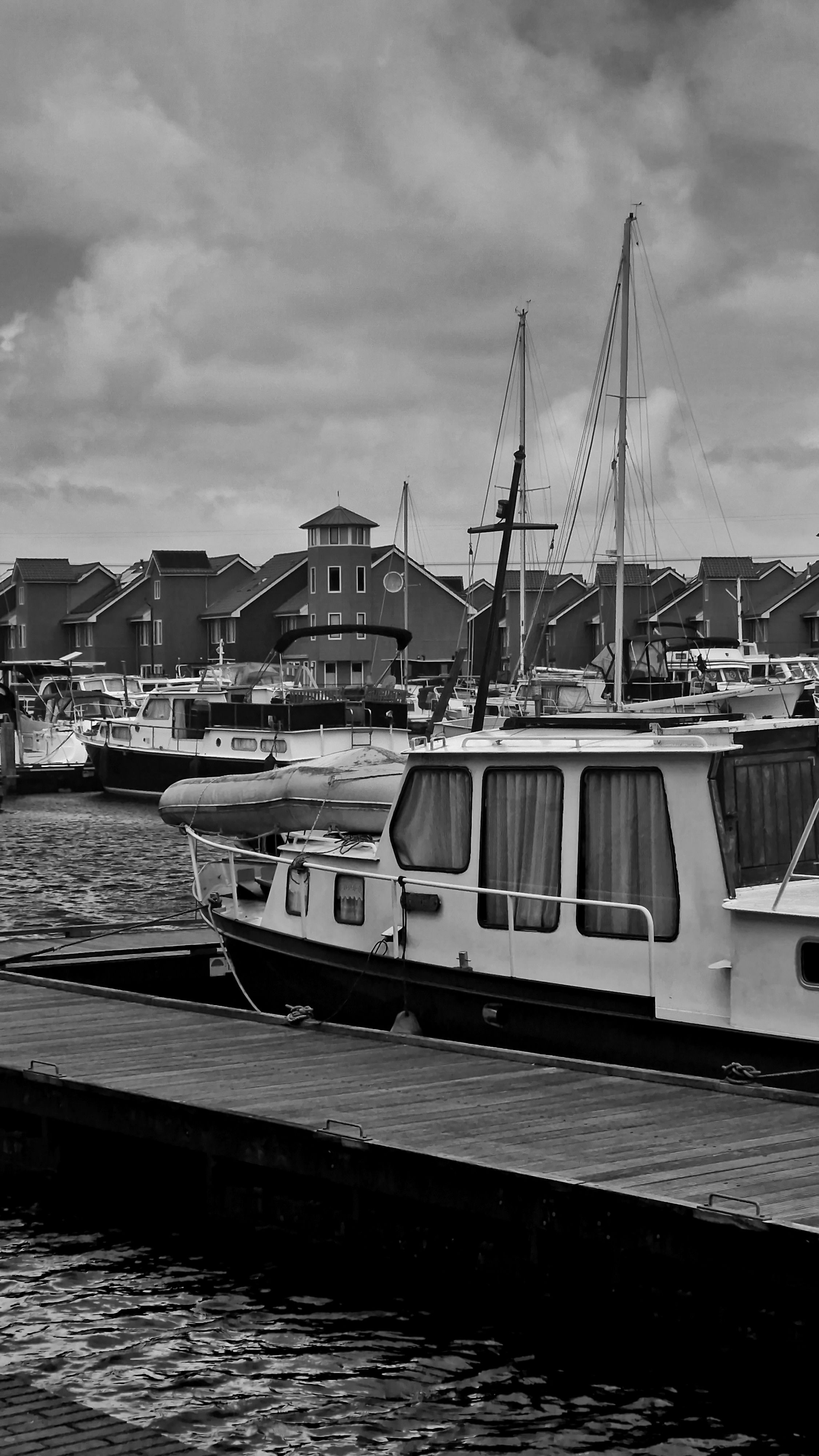 Black and white photo of boats docked at a marina with buildings in the background.