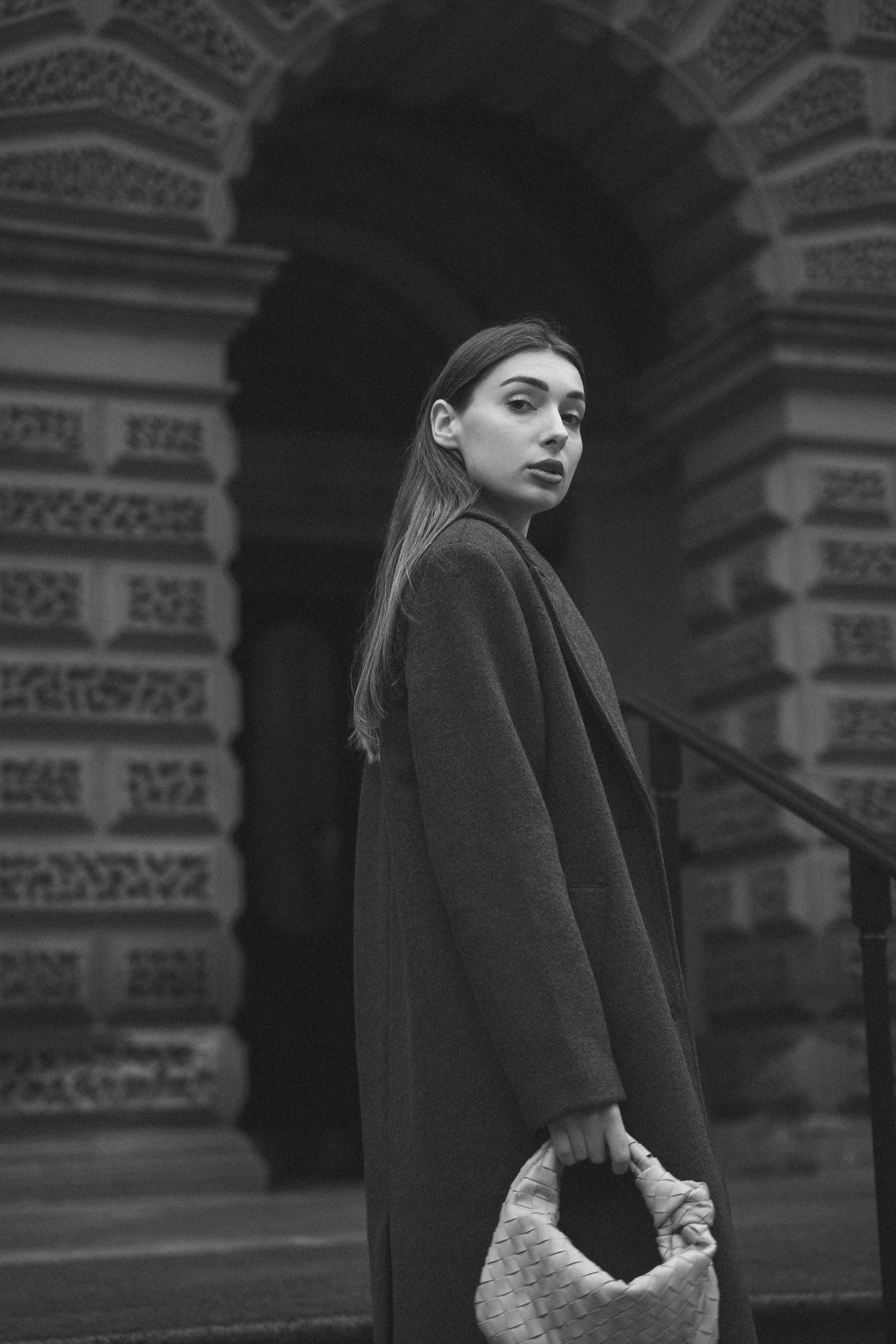 Male model wearing a tailored dark overcoat in a clean urban setting.