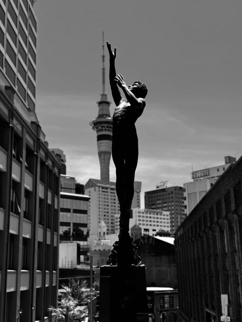 Black and white photo of Auckland with Sky Tower and sculpture in the foreground.