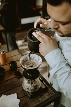 A barista carefully brews coffee using the pour over method in a cozy café setting.