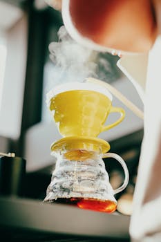 Steaming hot coffee brewed with a yellow dripper over a glass jug, captured indoors in Baku.