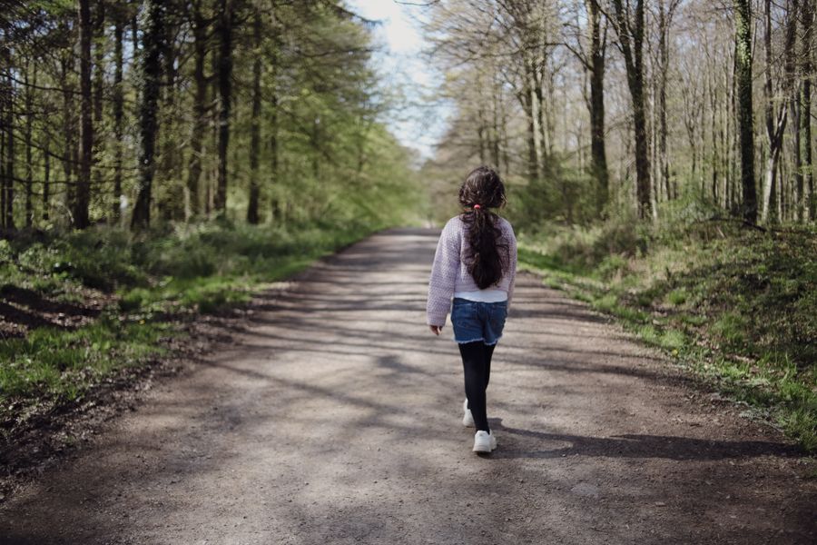 A young girl walks down a serene forest path surrounded by spring greenery.