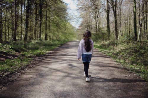 Free A young girl walks down a serene forest path surrounded by spring greenery. Stock Photo
