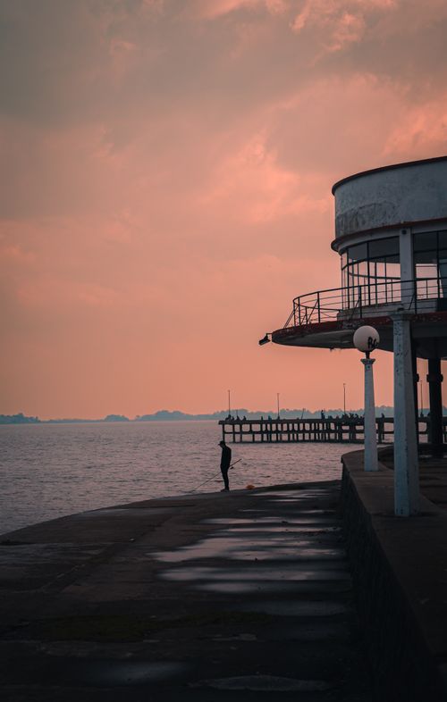 Free Silhouetted figure by a seaside structure during a dramatic sunset, evoking solitude and tranquility. Stock Photo