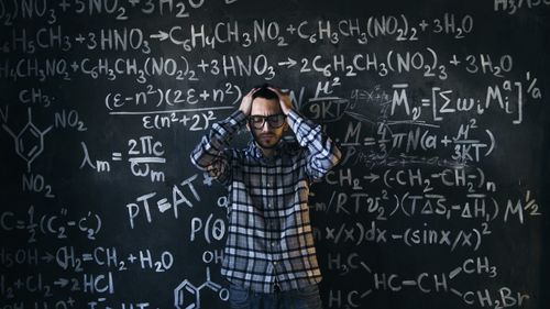 Man in glasses focusing on math problems on a blackboard
