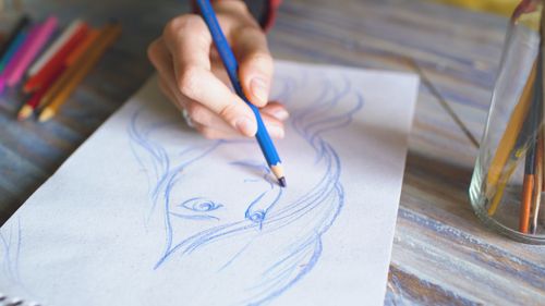 Free Close-up of a hand drawing a portrait using color pencils on paper. Stock Photo