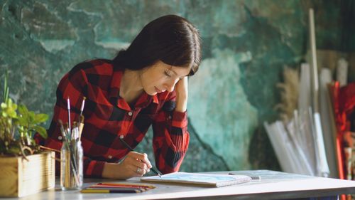 Free Concentrated woman in checkered shirt sketching with pencils in a vibrant art studio Stock Photo