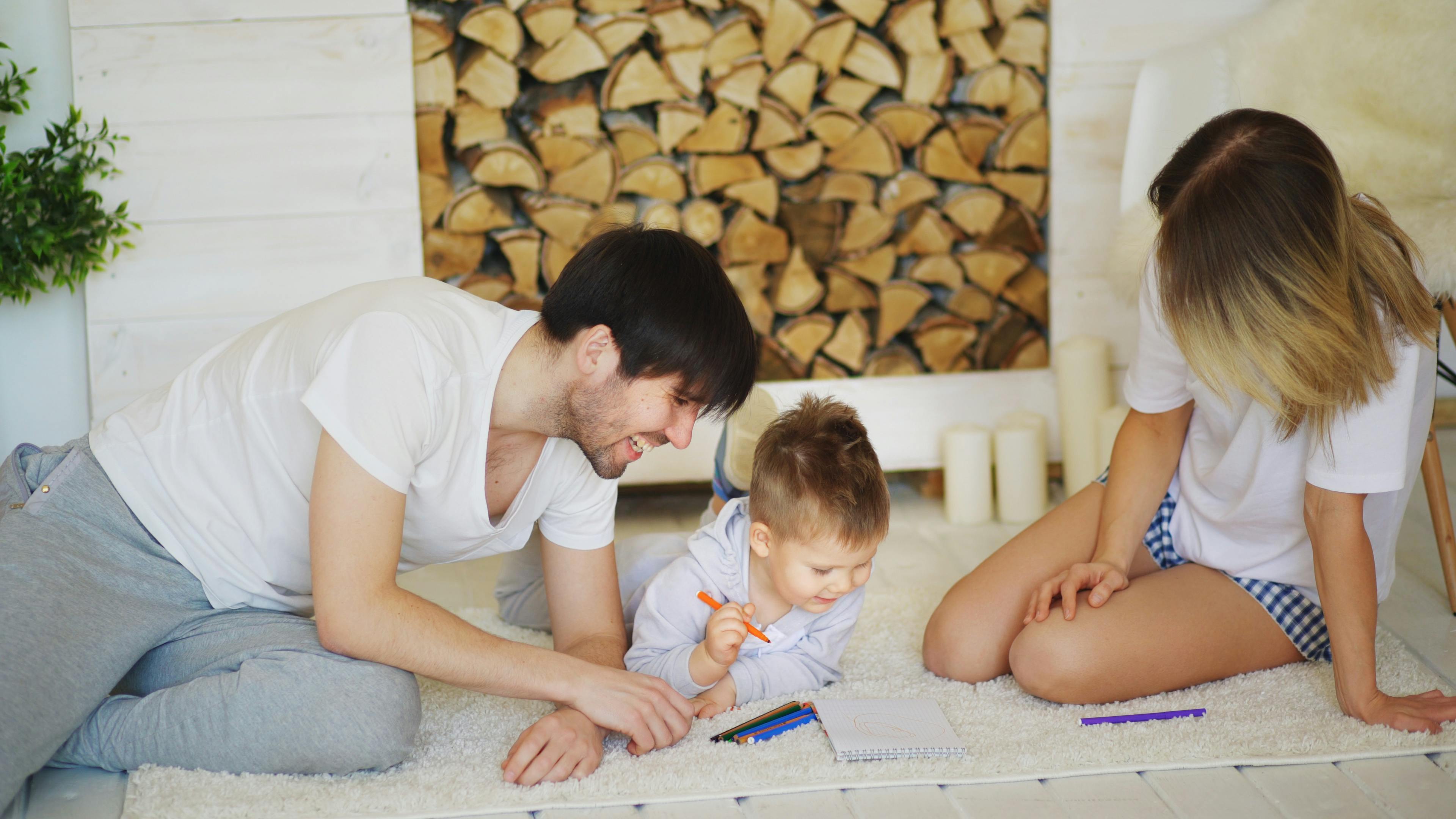 father and mother helping their child draw picture in their living room